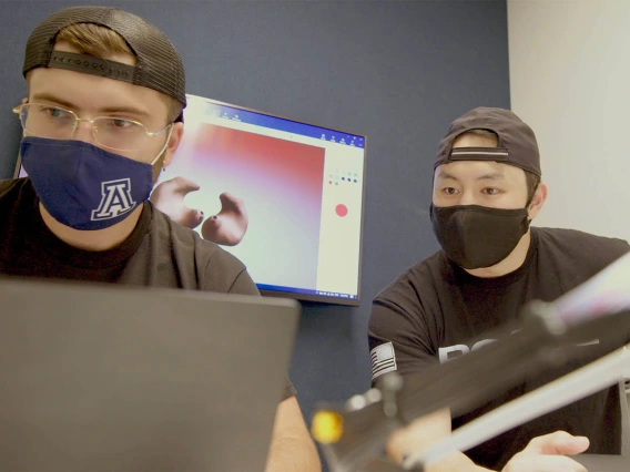 two students with backward facing hats and masks looking at a laptop screen