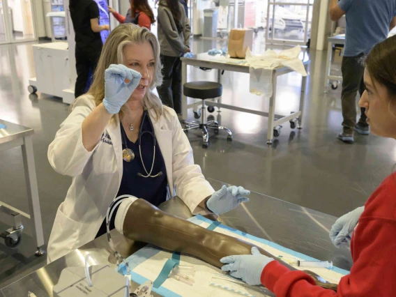 Female medical instructor working with students and patient in simulation setting.